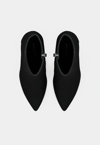 Botas de tobillo negras con punta afilada y parte superior de tela suave. Cuentan con un cierre lateral con acentos metálicos. Suelas planas y sin patrones visibles.