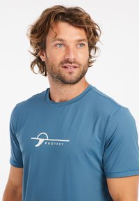 Blaues T-Shirt mit kurzen Ärmeln, das eine subtile gerippte Textur und ein weißes Logo auf der Brust zeigt. Es hat einen runden Halsausschnitt und atmungsaktives Material.