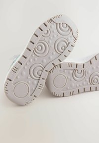 Suelas de zapatillas blancas con un patrón texturizado que presenta diseños circulares y punteados. Material de goma con acentos circulares elevados y surcos.