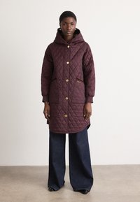 Gequilte lange jas in donkerburgundy, voorzien van een capuchon, knopen aan de voorkant, twee zijzakken en gouden hardware accenten. Textuurstof.
