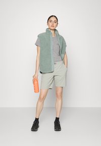 Light green fleece vest over a gray t-shirt, paired with light shorts and black shoes. Holding a coral water bottle. Simple design.