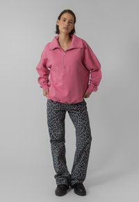 Rožinė medvilninė zip-up džemperis su dideliu apykakle; pilki kelnės su juodu leopardiniu raštu; masyvūs juodi batai.