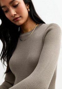 Geribbelde lange mouw top in taupe grijs, met een ronde halslijn. Accessoires zijn onder andere een gelaagde ketting en oorringen.