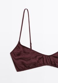 Bralette bourgogne avec des bretelles fines, une finition texturée, des bonnets triangulaires et des détails cousus le long des bords.