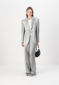 Lysegrå skreddersydd dress med en strukturert blazer og vide bukser. Glatt stoff med subtil glans, sammen med en liten svart håndveske.