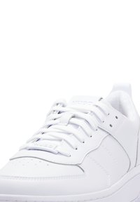 Baskets blanches en matériau synthétique lisse, avec un design à lacets, une boîte à orteils perforée et un branding subtil sur la languette.