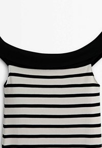 Haut sans manches à rayures horizontales noires et blanches avec un large col noir et des bretelles sur un fond blanc.