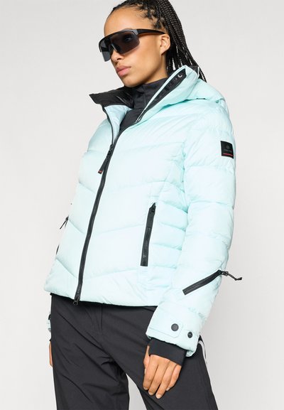 Ανοιχτό μπλε μπουφάν με χνουδωτή υφή και μαύρο εσωτερικό, διαθέτει λάστιχα με φερμουάρ, κουκούλα και ρυθμιζόμενους καρπούς. Κατασκευασμένο από υλικό με γυαλιστερή υφή.