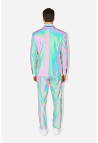 Iridescent pak met reflecterend materiaal, een aansluitend ontwerp en bijpassende broek met een gladde textuur. Draagt witte schoenen.