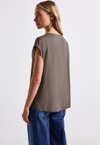 Top marr�ón de manga corta con un ajuste holgado y textura suave. Combinado con jeans azules de pierna ancha, visto desde la parte de atrás, mostrando un diseño sencillo.