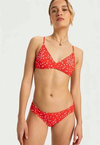 Rotes Bikini-Set bestehend aus einem dreieckigen Oberteil mit weißen Blumenmustern, verstellbaren Trägern und passendem Unterteil mit seitlichen Raffungselementen.