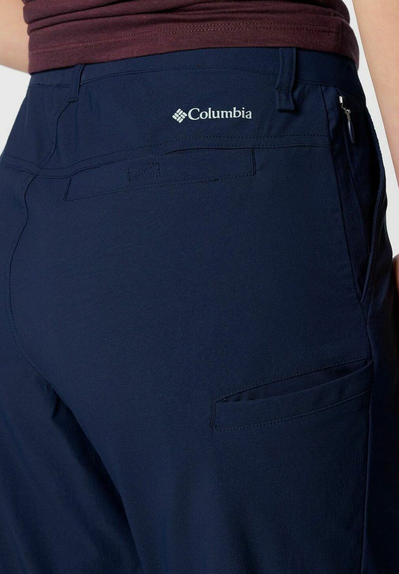 Granatowe spodnie Columbia z gładką fakturą, z tylnymi kieszeniami i logo na pasku, zaprojektowane z myślą o aktywnościach na świeżym powietrzu.