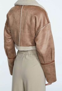 Korte jas van zachte, bruine nep-suède met een crème kleurige fleece kraag en details. Voorzien van brede mouwen en een relaxte pasvorm, gecombineerd met beige broek.