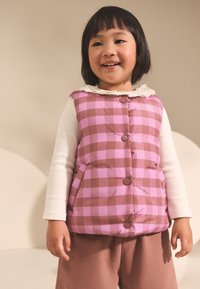 Polstret vest i lyserødt og brunt ternet mønster med brune knapper, rundet krave og en hvid skjorte med lange ærmer under.