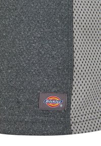 Grå tekstil med en teksturert overflate til venstre og et lysegrå mesh med svarte prikker til høyre. Har et sydd "Dickies"-merke.