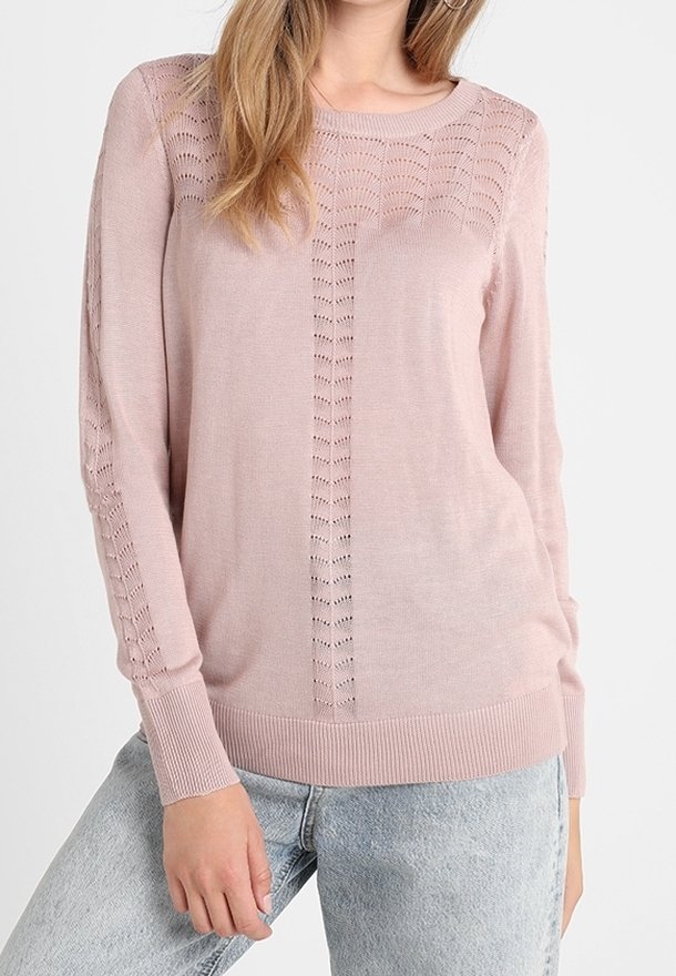 Femme portant un pull en maille rose clair avec des motifs verticaux ajourés sur les manches et le devant, associé à un jean bleu clair.