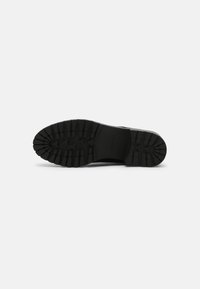 Black rubber outsole with deep treads for traction. Rounded toe shape and smooth surface. Features embossed branding near the heel.