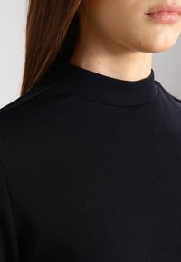 Top nero a collo alto realizzato in tessuto testurizzato. Presenta un design aderente e una finitura liscia, senza pattern o decorazioni visibili.