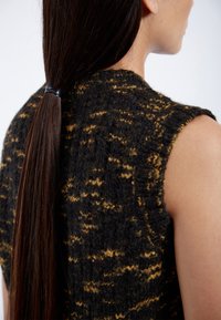 Stickad ärmlös tröja i svart och gult med ett texturerat, vågigt mönster. Materialet ser fluffigt ut med en synlig sömdesign.