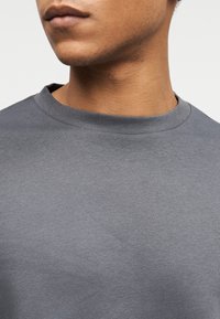 Γκρι βαμβακερό μπλουζάκι με κλασικό στρογγυλό λαιμόκοψη, με λεία υφή και κοντά μανίκια, εμφανιζόμενο από το στήθος και πάνω.