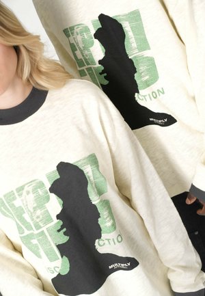 Deux personnes portant des chemises à manches longues crème avec des cols noirs, un grand graphique silhouette noir et un texte vert affichant "EXPERT" et "MULTIPLY APPAREL."