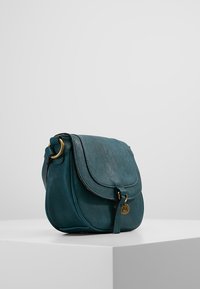 Turkusowa skórzana torba na ramię z klapką, zaokrąglonym kształtem, bocznym przeszyciem i złotym akcentem metalowym. Miękka faktura z zaokrąglonymi krawędziami.