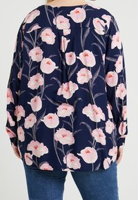 Blusa blu navy con un motivo floreale caratterizzato da fiori rosa e gambi verdi. Maniche lunghe, vestibilità rilassata e scollo rotondo.