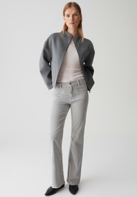Graue Wollbomberjacke mit hohem Kragen, kombiniert mit hellgrauen, ausgestellten Jeans und schwarzen, spitzen Stiefeletten. Glatte, strukturierte Textur.