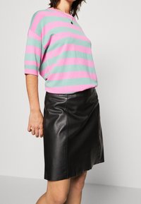 Pull rayé rose et turquoise, manches courtes, assorti à une jupe en cuir noire, texture lisse, coupe ajustée.