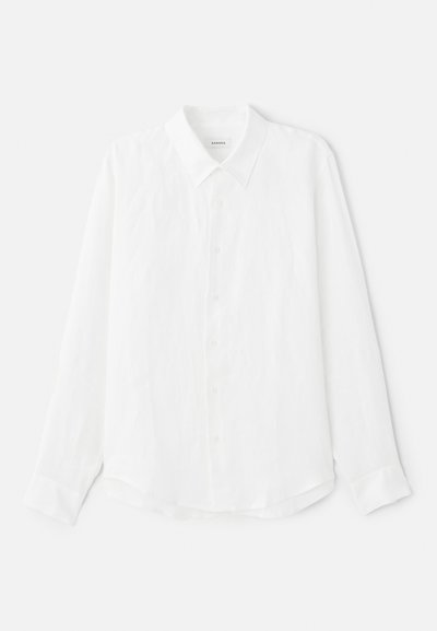 Valkoinen pitkähihainen paita, joka on valmistettu pellavasta. Paidassa on klassinen kaulus, edessä napitus ja sileä pinta. Helma on hieman kaareva.