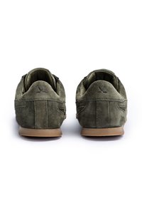 Para oliwkowo-zielonych zamszowych sneakersów widzianych od tyłu, z jasnobrązowymi podeszwami i naszytym logo na pięcie.