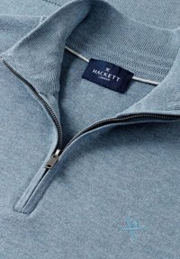 Svetlomodrý sveter s golierom na štvrťzips, textúrovaným golierom, viditeľným kovovým zipsom, štítkom Hackett London a malým vyšívaným logom na hrudi.