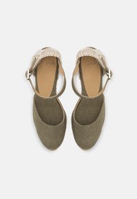 Grønne lerret espadriller med en vevd beige stropp og ankelreim. Rund tå, flat såle, teksturert stoff. Minimalistisk og funksjonelt design.