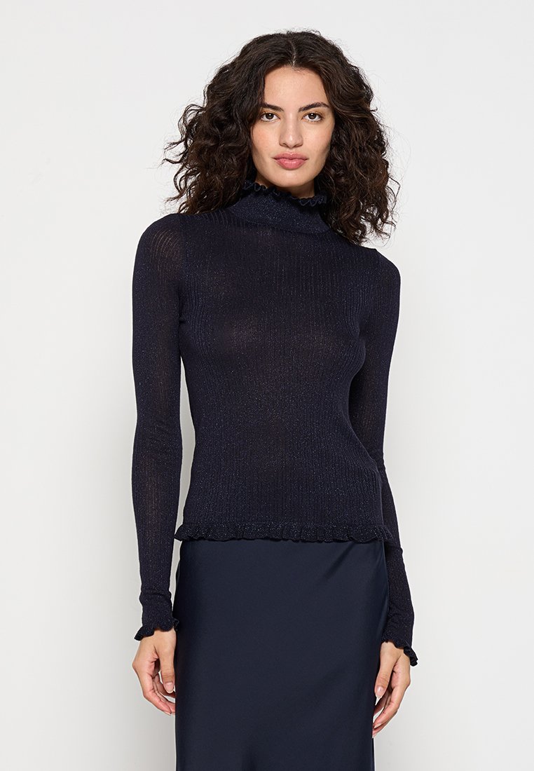 Haut à manches longues en marine avec texture côtelée, présentant un col montant et un ourlet ondulé. Tissu doux et léger avec un léger scintillement.