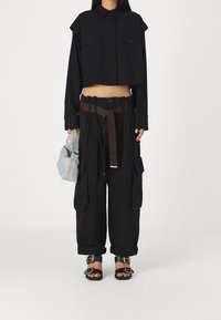 Černé zkrácené tričko s předním knoflíkovým zapínáním a náprsními kapsami, spárované s volnými černými cargo kalhotami s hnědým páskem a několika kapsami.