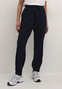 Mörkblå taperade joggerbyxor med dragsko i midjan, två sidofickor och elastiska muddar. Lättviktsmaterial med en mjuk yta.