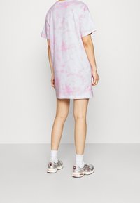 Sukienka T-shirt w tie-dye w pastelowych odcieniach różu i fioletu, krótkie rękawy, luźny fason, zestawiona ze srebrnymi trampkami i białymi skarpetkami do kostek.