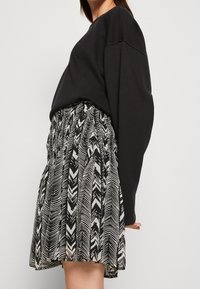 Sweatshirt noir surdimensionné associé à une jupe noire et blanche à motif zigzag et taille froncée.