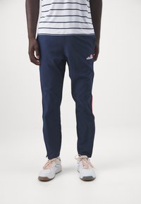 Marina blå träningsbyxor med röda sidostenar, tillverkade av ett smidigt och lätt material. Har en broderad logotyp och en avsmalnande design.