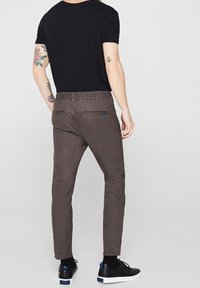 Celana abu-abu gelap dengan pinggang elastis, potongan slim, dan dua saku belakang, dipadukan dengan kaos hitam lengan pendek dan sepatu sneaker hitam.