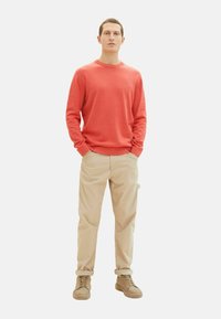 Rød langærmet sweater, beige bukser og lysebrune sko. Afslappet pasform med ribbede manchetter og kant. Enfarvede uden mønstre.