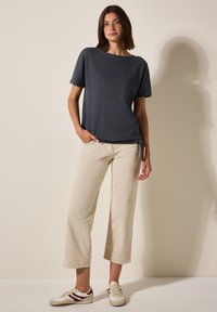 Haut à rayures marine à manches courtes, coupe décontractée, associé à un pantalon large beige clair et des baskets blanches avec des accents rouges.