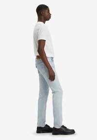 Helle blaue Jeans im Slim-Fit-Schnitt, aus Baumwolle, mit Fünf-Taschen-Design, braunem Lederpatch am hinteren Bund, kombiniert mit schwarzen Schuhen.