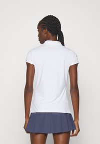 Polo bianco con colletto, maniche corte e spacchi laterali, abbinato a una gonna a pieghe blu navy con un motivo testurizzato.