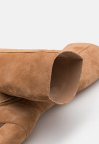 Bottes chevilles en daim marron avec un bout arrondi et un design à tige ouverte, dotées d'une doublure lisse et de détails de couture subtils.