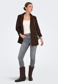 Bruine suède blazer met een reverskraag, zwarte manchetten, gecombineerd met grijze skinny jeans en donkerbruine cowboylaarzen. Zilveren ketting schoudertas.