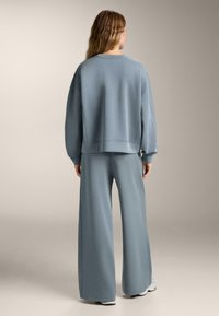 Ljusblå sweatshirt och matchande vida sweatpants i ett mjukt material. Har ribbade muddar och en avslappnad passform med sömmar.