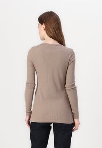 Maglietta a maniche lunghe a coste color marrone chiaro, con scollatura rotonda e design aderente, abbinata a jeans scuri, vista da dietro.