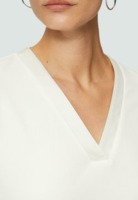 Witte v-hals top met een gladde textuur en subtiele glans. De halslijn heeft een contrasterende afwerking die het elegante ontwerp benadrukt.