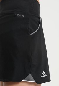 Jupe de sport noire Adidas Climalite avec poche latérale et détail en mesh à l'ourlet portée sur la partie inférieure du corps d'une personne.
